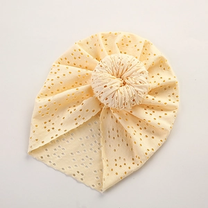 Close-up of cream lace hollow baby beanie with donut knot and breathable mesh texture