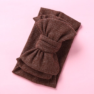 Detail view of dark brown ribbed knit baby headband with oversized bow on pink backdrop