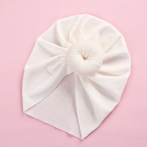 Close-up of white newborn donut turban hat with ribbed knit texture on pink background