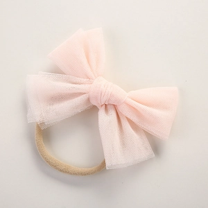 Detail of soft pink layered tulle bow on a seamless beige elastic nylon baby headband