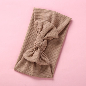 Brown ribbed knit baby headband with a large bow on a soft pink background