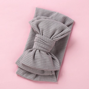 Close-up of gray ribbed knit baby headband with oversized bow on pink background