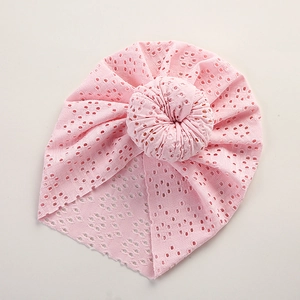 Detail of baby pink lace beanie with breathable hollow design and large bun knot
