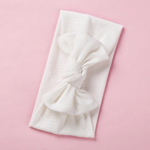 Close-up of white ribbed knit baby headband featuring a large elastic cotton bow
