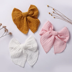 Three muslin cotton bow hair clips in ginger, pale pink, and white on a natural background