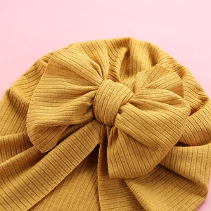 Ginger yellow baby turban headwrap with large ribbed bow on a soft pink background
