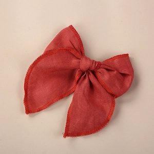 Détail du nœud papillon en lin rouge montrant le bord brodé et la texture du tissu fin