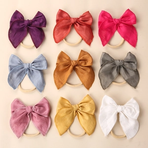 Flat lay of nine colorful linen bow headbands for baby girls on a beige background