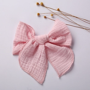 Detailed close-up of a pink muslin bow clip with soft textured cotton gauze fabric