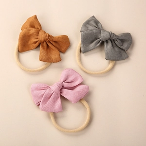 Detailed texture of three linen bow headbands in yellow, grey, and soft pink for babies