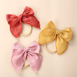 Detail of baby linen bow headbands in brick red, mustard, and pink with nylon bands