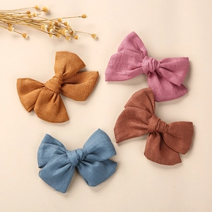 Vue à plat de quatre barrettes nœuds en lin en moutarde, rose, bleu et brun avec fleurs
