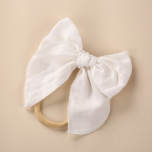 Detail of white linen bow headband with embroidered edges and nude elastic nylon hair tie