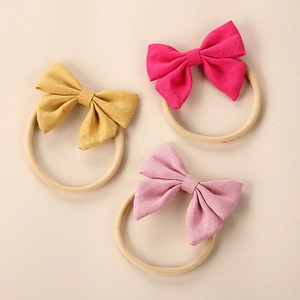 Detailed texture of three linen bow headbands in yellow, magenta, and soft pink for infants