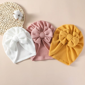 Detail of baby waffle knit bow beanies in white, pink and yellow soft fabric textures