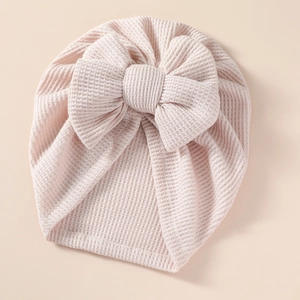 Detail of baby pink waffle knit beanie featuring a large soft decorative double bow