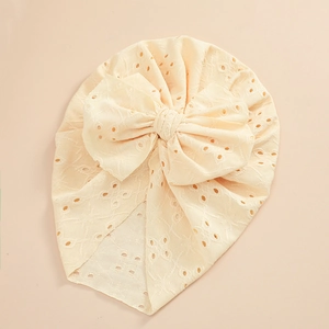 Detail of baby turban hat featuring eyelet embroidery and a large bow in cream white
