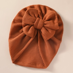 Detailed close-up of a ribbed knit baby hat with a large bow in caramel brown tone