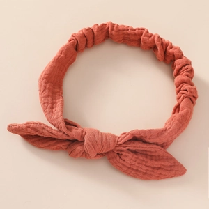 Close-up of baby cotton headband with bow knot and breathable textured fabric in rust red