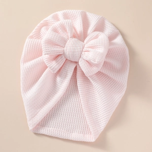 Close-up of baby waffle knit hat in light pink with a large decorative soft bow detail