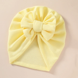 Close-up of baby turban hat featuring yellow waffle knit fabric and a large bow