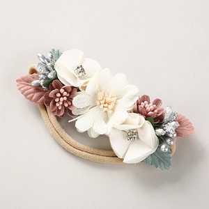 Detail eines Baby-Stirnbands mit 3D-Stoffblumen, Strasssteinen und grünen Blättern