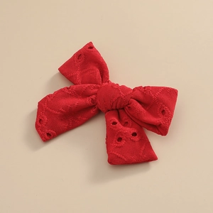 Détail de la barrette à nœud rouge en dentelle brodée montrant la texture du tissu ajouré