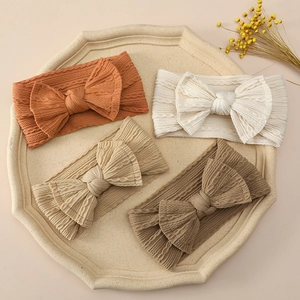 Soft nylon baby headbands with large bows in four earthy colors on a ceramic tray