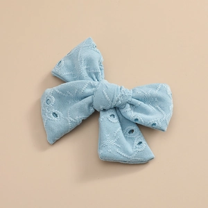Détail d'une pince à cheveux avec nœud en dentelle bleue et motifs brodés ajourés