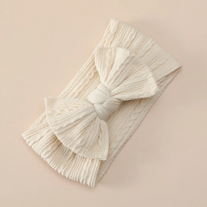 Detailed texture of soft cream jacquard nylon headband with large knit bow for infants