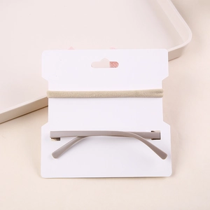 Minimalist beige elastic bow headband and taupe hair clip set on a white display card
