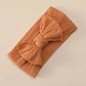 Close-up of caramel brown baby headband with cable knit texture and large bow detail