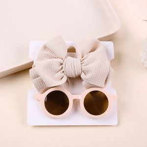 Detail view of baby bow nylon headband and round pink sunglasses on a white display card