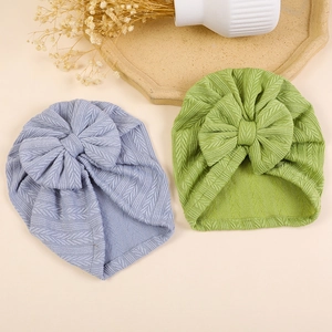 Baby knit turban hats with big bows in lavender and green colors on warm background