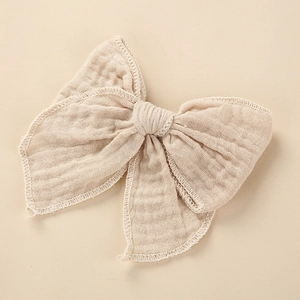 Detail of soft cotton muslin hair bow with white overcast stitching and crinkle texture