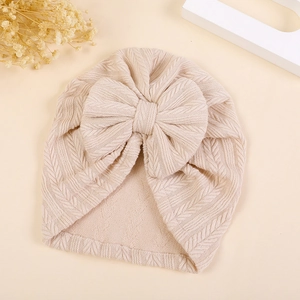 Close-up of beige knitted baby turban with herringbone pattern and bow detail