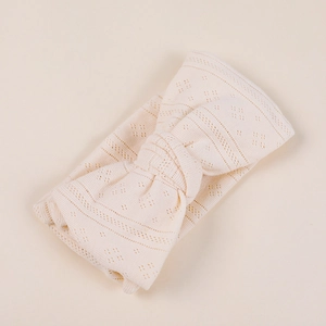 Close-up of cream knitted baby headband with hollow texture and bow detail
