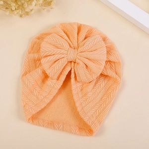 Detail of warm orange knitted baby turban hat with wheat ear texture and large bow