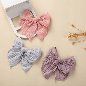 Three cotton muslin bow hair clips for babies in soft pink, blue, and purple pastel colors