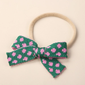 Detailed close-up of knitted floral bow headband for babies with soft nylon band