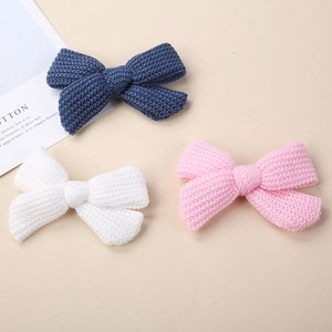 Close-up of three knitted bow hair clips in navy, white and pink with fine wool texture