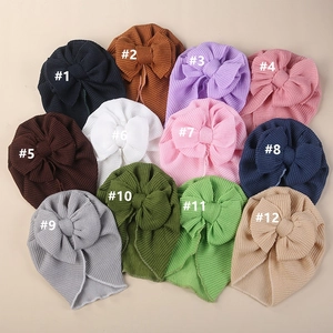 Flat lay collection of twelve colorful waffle knit baby turban hats with large bows