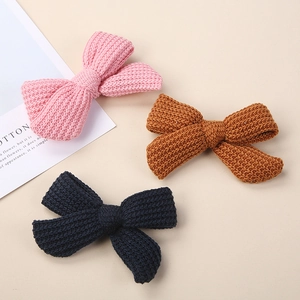Detailed close-up of three knitted bow hair clips in pink, caramel, and navy blue tones