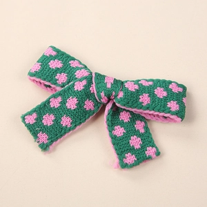 Dettaglio di un fermaglio per capelli a fiocco in maglia verde e rosa ricamato