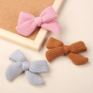 Three knit bow hair clips in pink, brown and grey for babies on a warm display background
