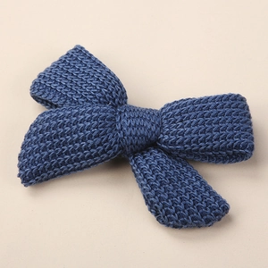 Macro shot of dark blue knitted bow hair clip showing detailed wool stitch texture