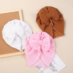 Detailed close-up of waffle knit baby turban hats with large bows in white, pink, and brown
