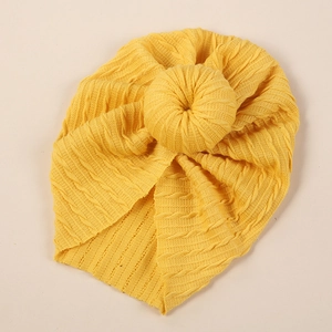 Detail of yellow cable knit baby turban hat featuring a large donut knot decoration