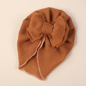 Detail of caramel knitted baby turban hat with oversized bow and ribbed texture