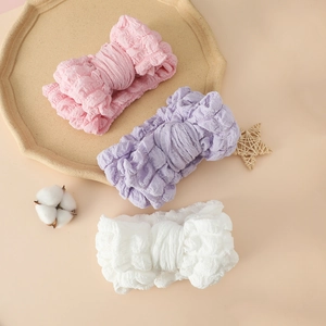 Détail de trois bandeaux à nœuds texturés rose, violet et blanc sur un plateau en pierre